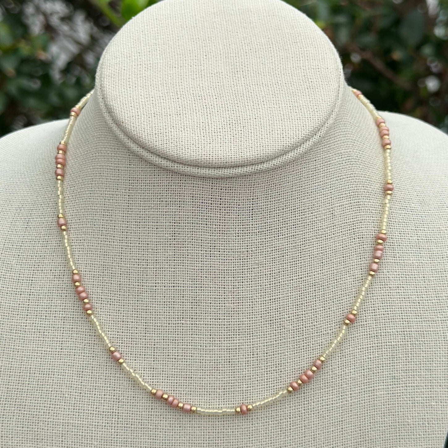 A dusty pink necklace with gold-filled beads displayed on a mannequin torso.