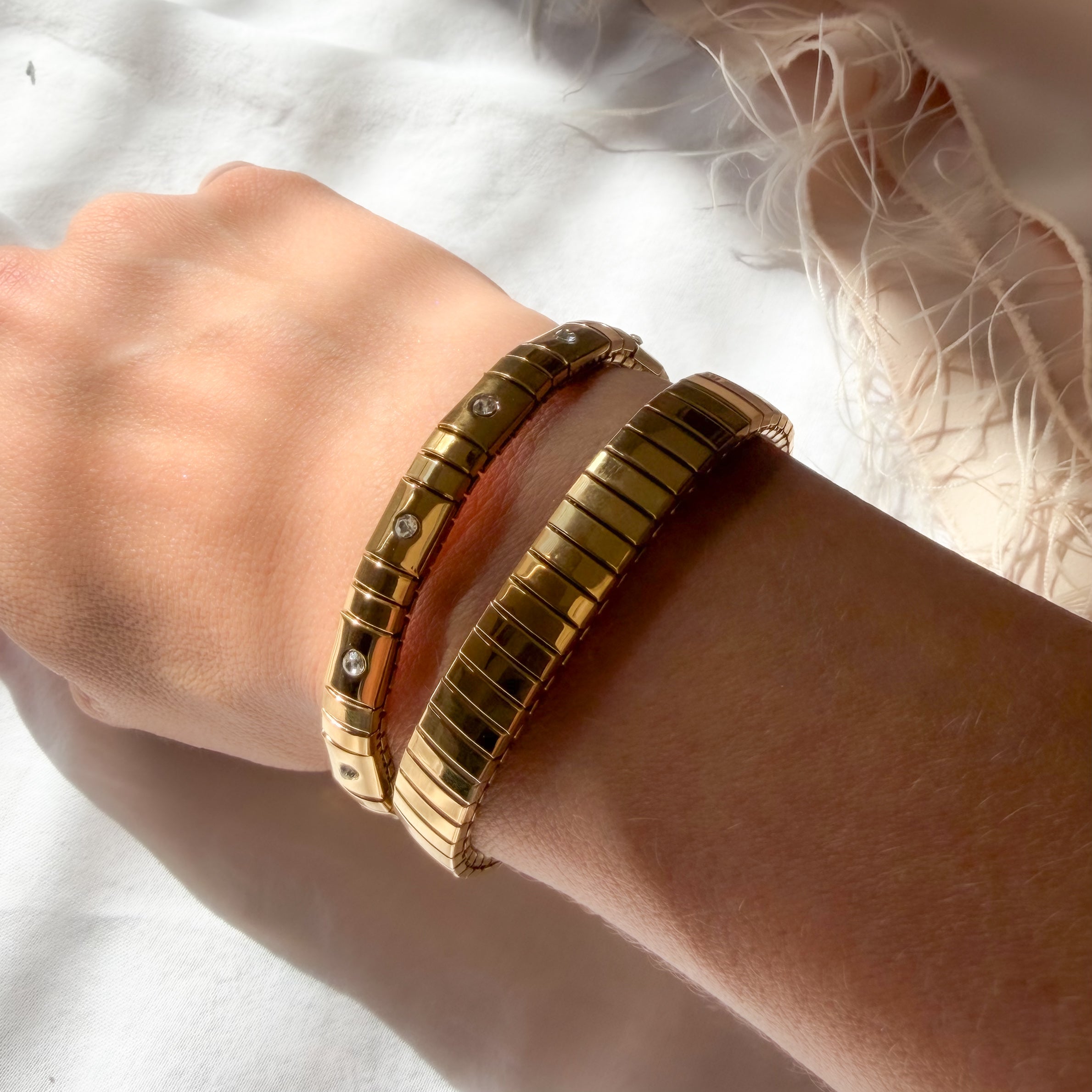 Gold bracelets on a wrist with a white background